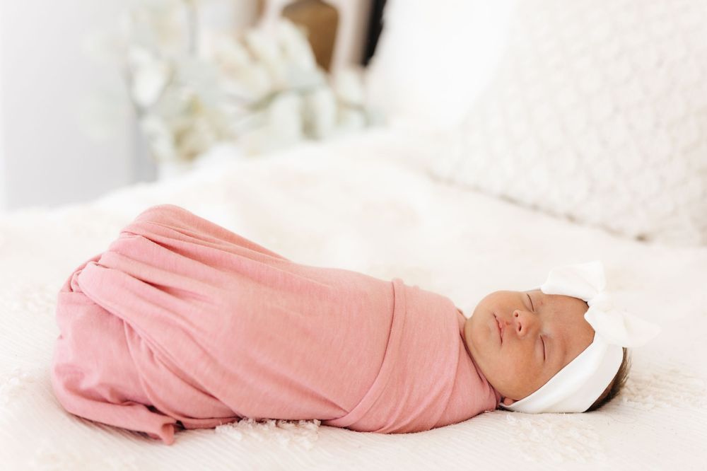 A baby lying swaddled in soft pink and white blankets sleeping peacefully against a neutral background. newborn photographer in utah newborn