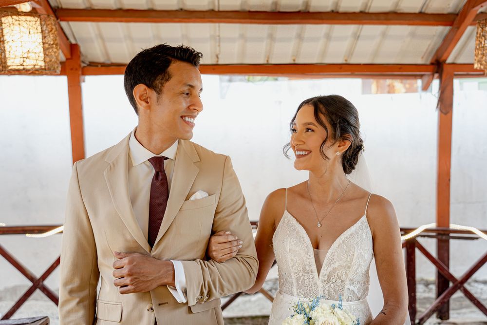 A couple in elegant wedding attire gazes at each other under a covered wooden patio during their destination wedding.