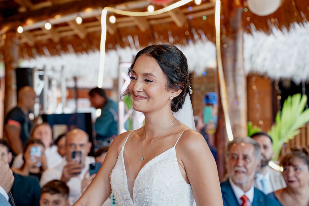 A joyful bride in a white spaghetti strap wedding dress smiles during her tropical beach wedding ceremony.