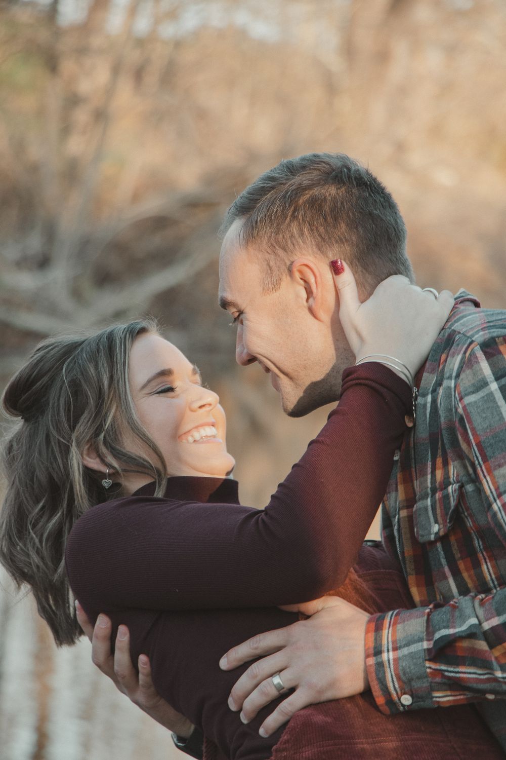 Couple laughs and looks into each other's eyes while embracing, surrounded by warm golden light.