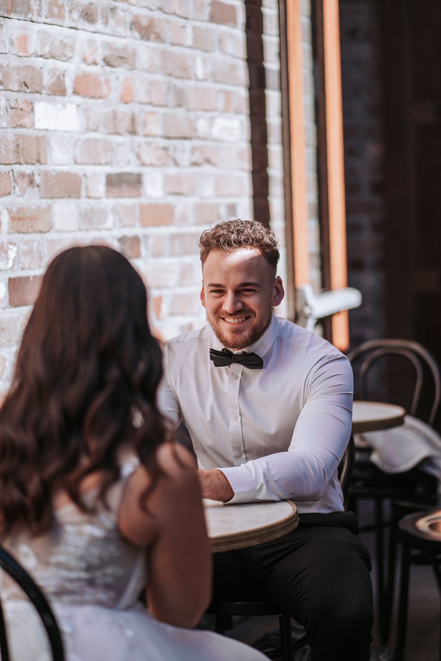Two people having a conversation at a cafe table with exposed brick wall in the background.