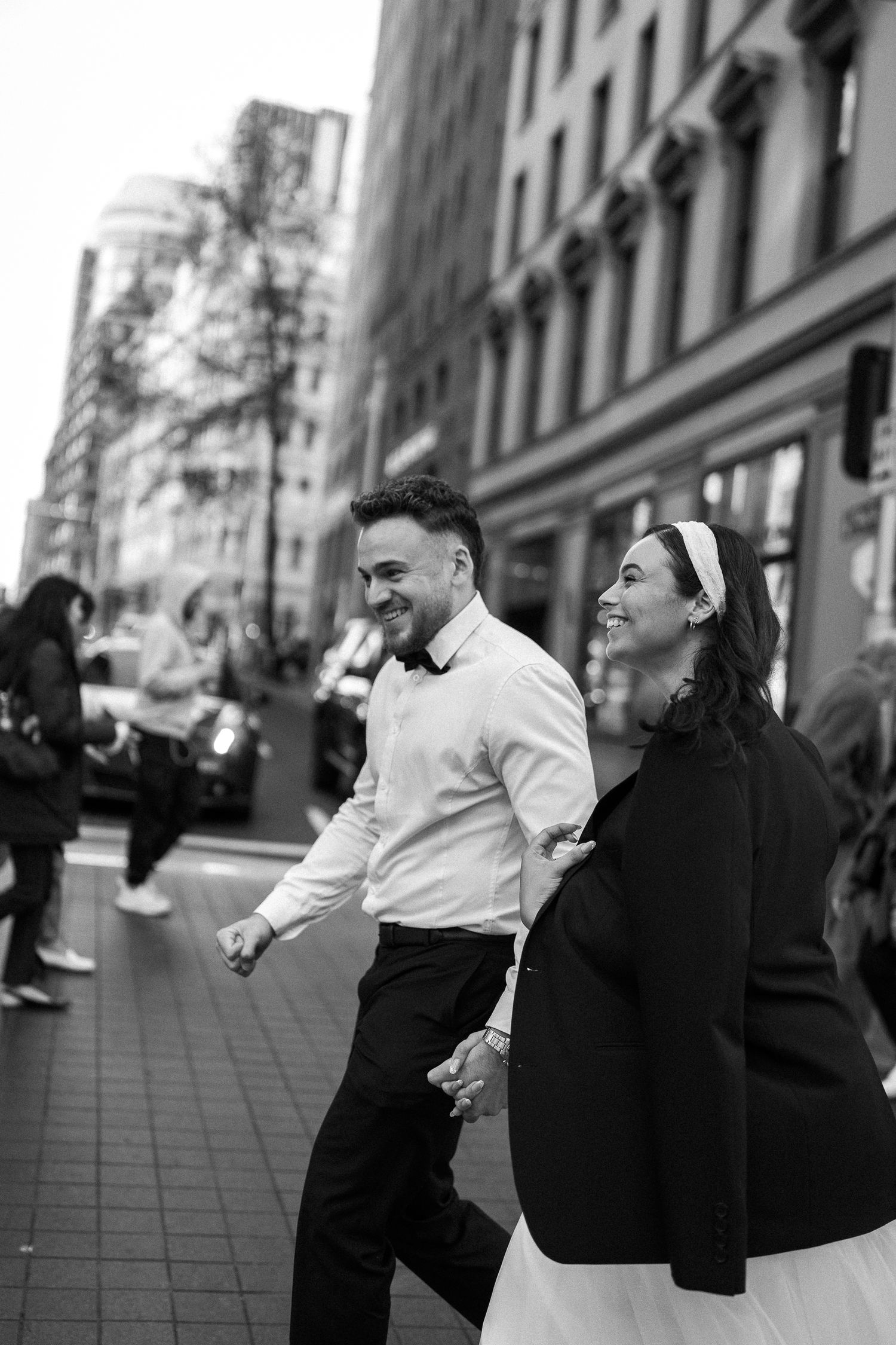 A couple laughs together while walking down a city street in black and white.