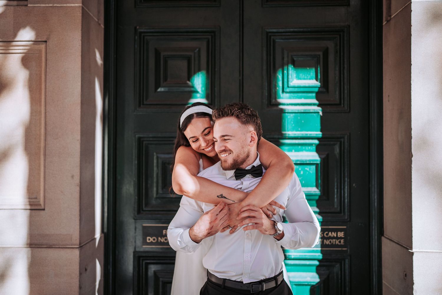 A sweet embrace shared between a couple in formal attire in front of a dark wooden door with turquoise light.