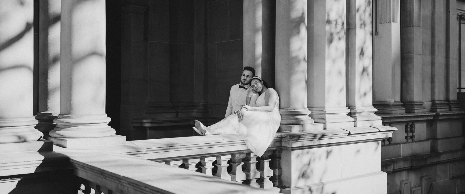 A person in black and white photograph sits on grand classical architectural steps surrounded by towering columns.