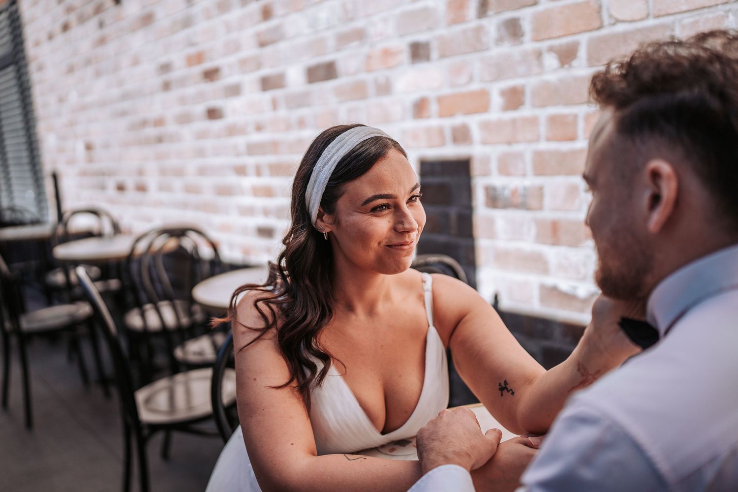 A couple seated at a restaurant table share an intimate conversation with exposed brick walls in the background.