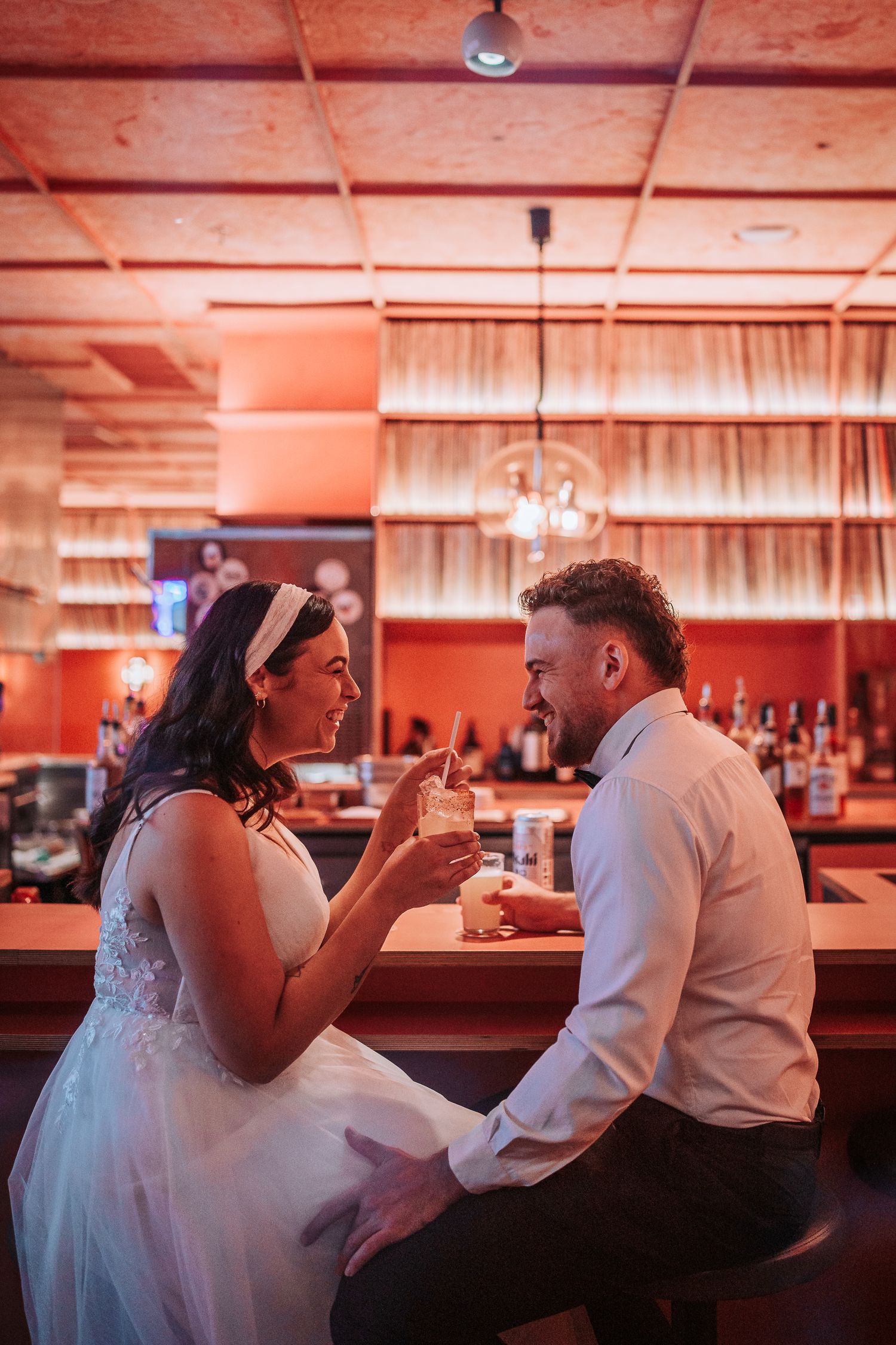 A couple shares milkshakes at a bar counter in a red-lit room with a romantic vintage atmosphere.