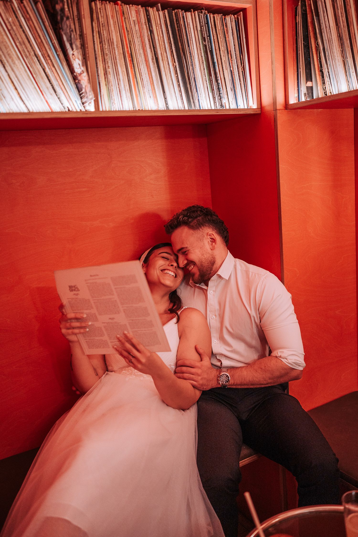 Couple sharing tender moment while reading documents together in red-walled room with vinyl record storage.