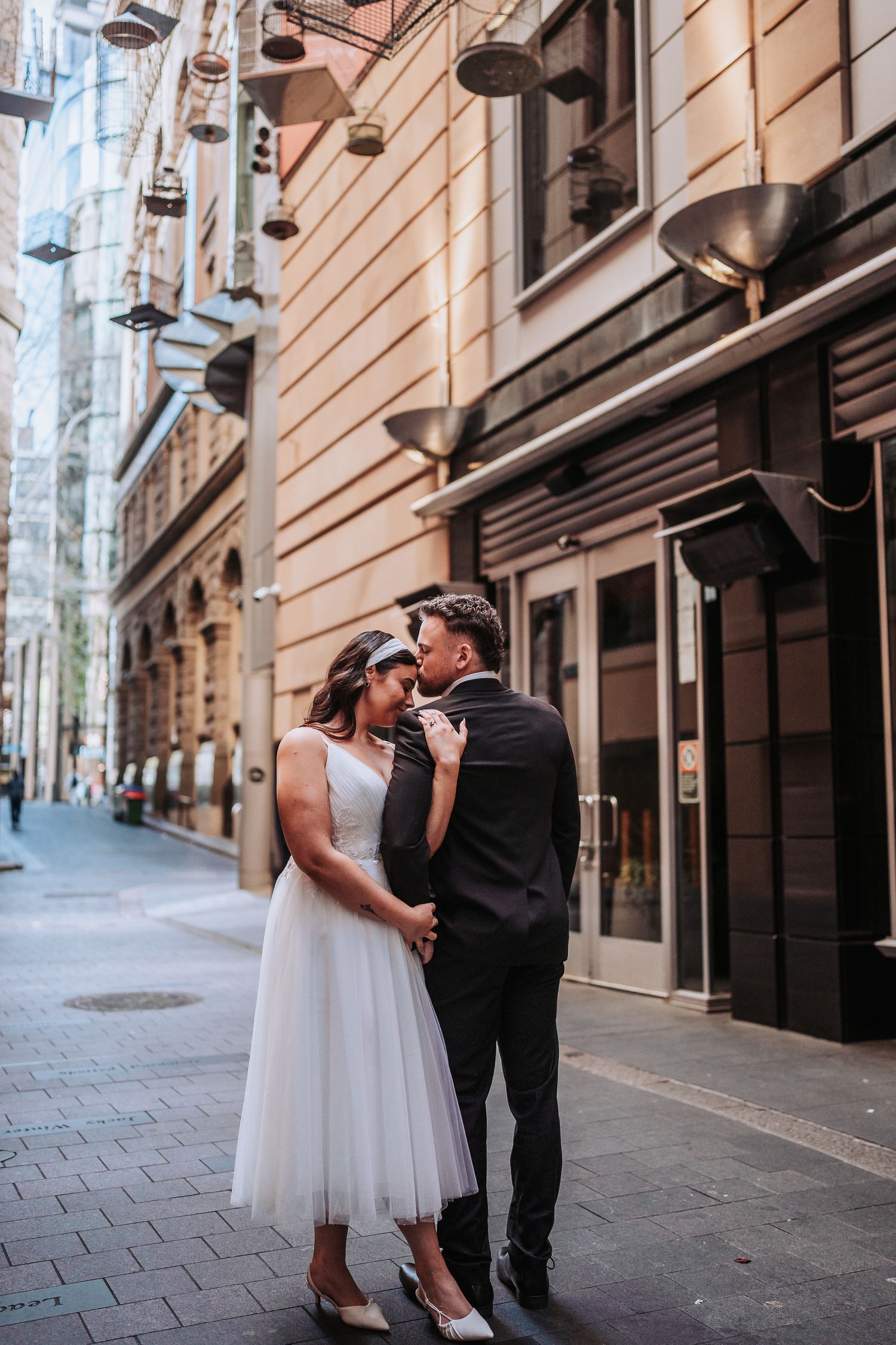 A romantic wedding couple shares tender moments in an elegant European city alleyway with historic stone buildings.
