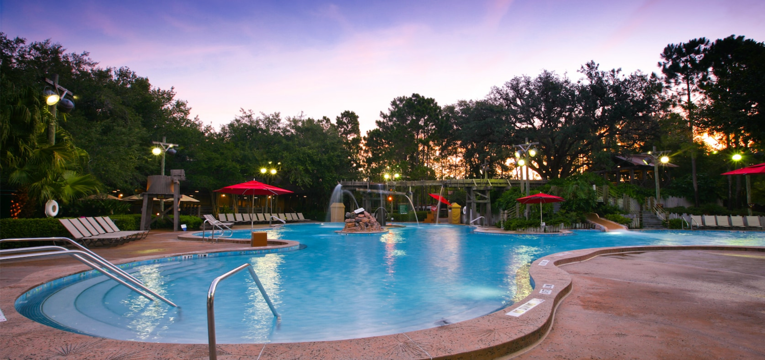 Evening view of illuminated resort pool area with water features.