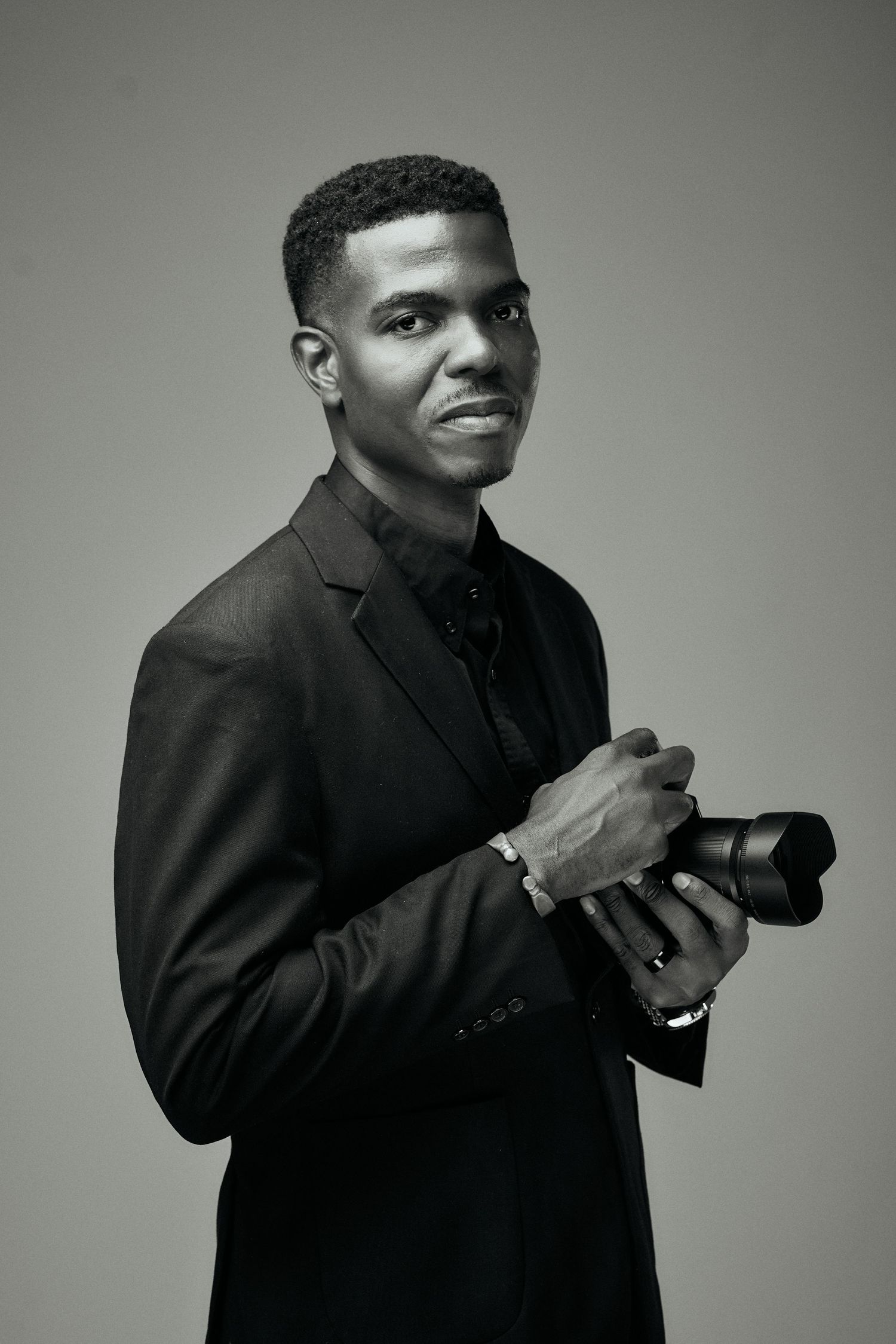 Professional photographer in black clothing takes photos with a vintage camera against a gray studio Jamaican Photographer
