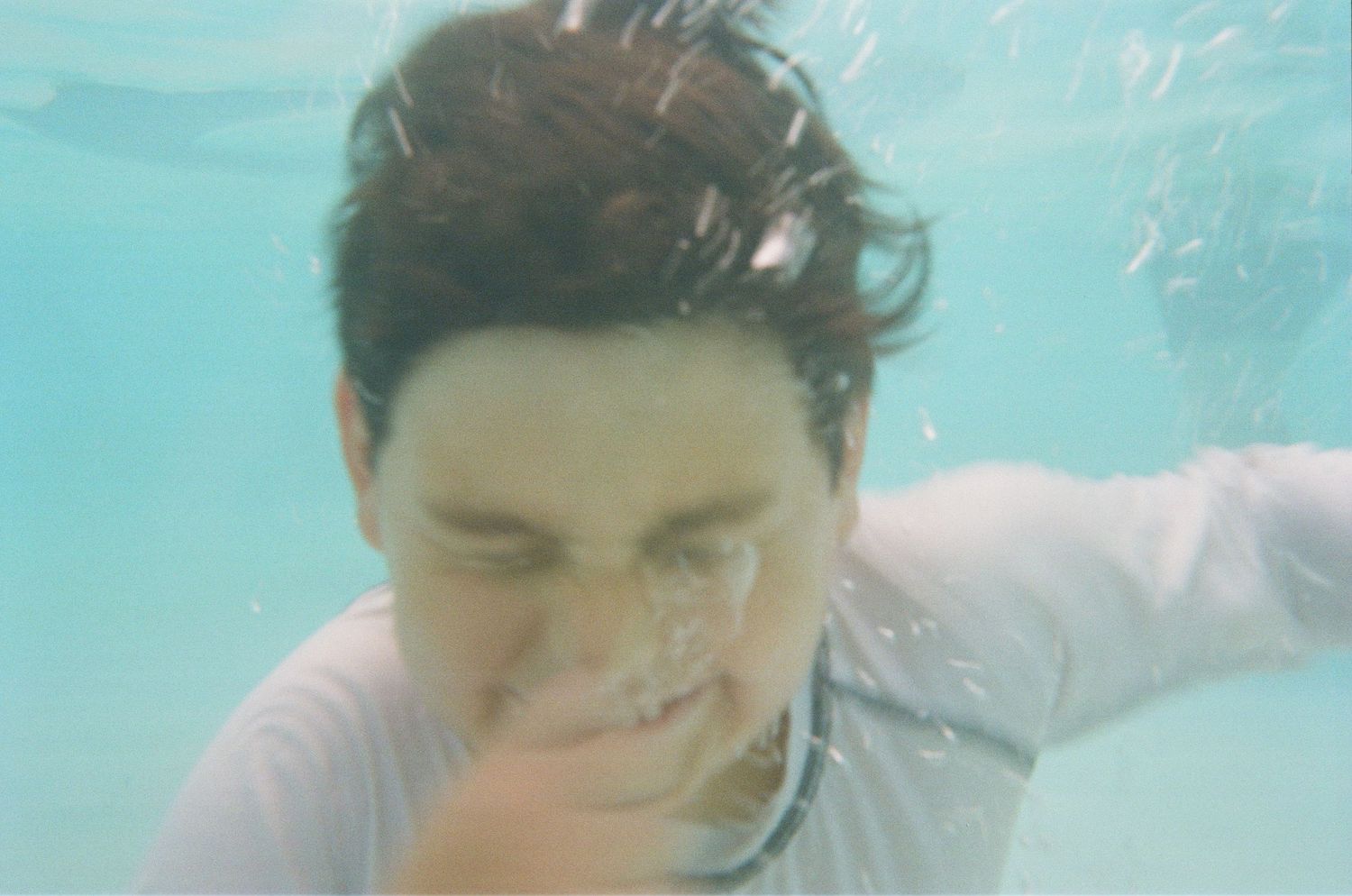 Person swimming underwater with closed eyes in turquoise blue water with flowing movement captured in dreamy style.