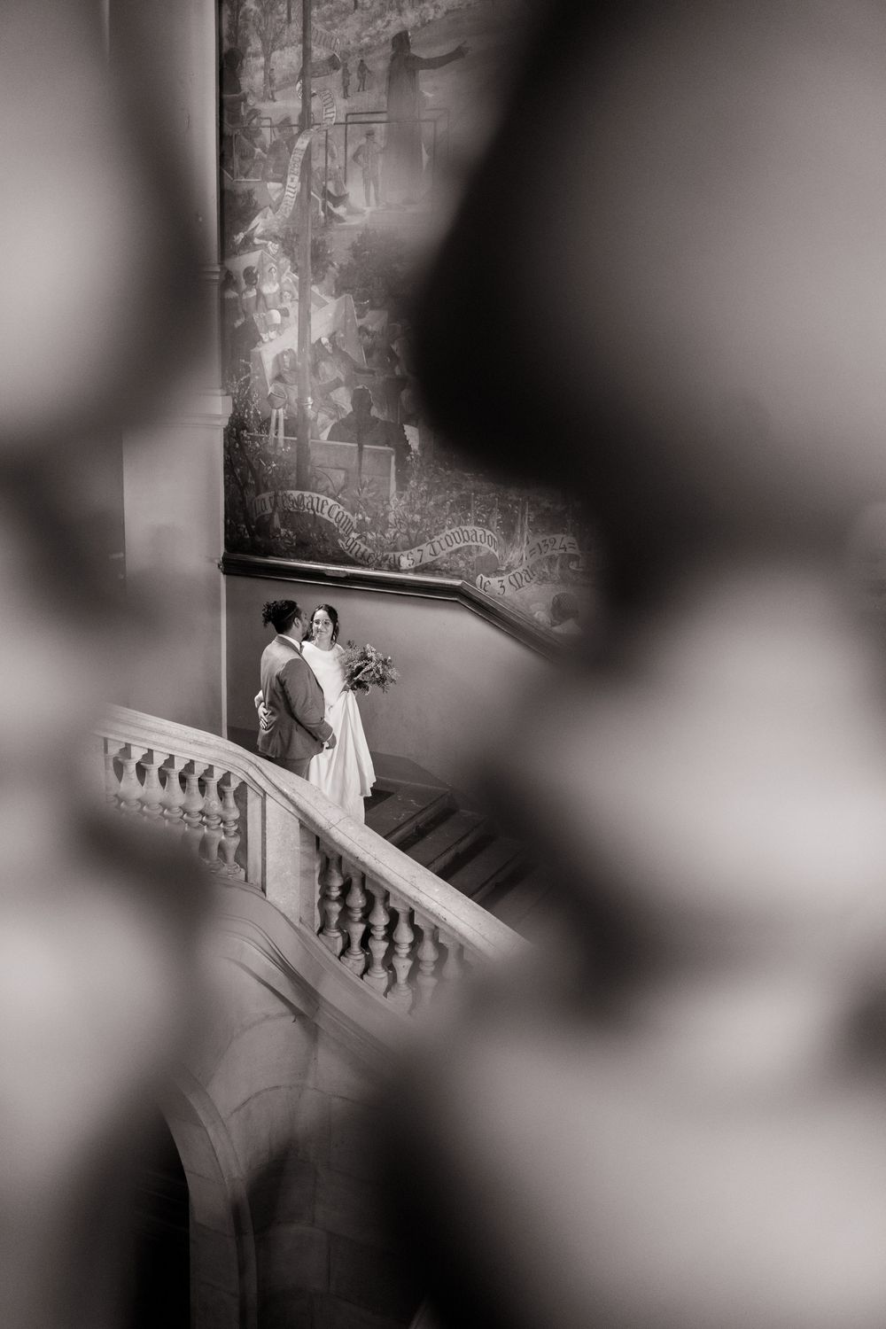 A romantic black and white wedding photo capturing a couple embracing on a grand staircase with dramatic lighting.