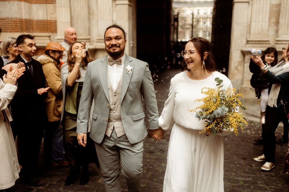 Happy newlywed couple walk past cheering guests outside a church on their wedding day in a joyful celebration.