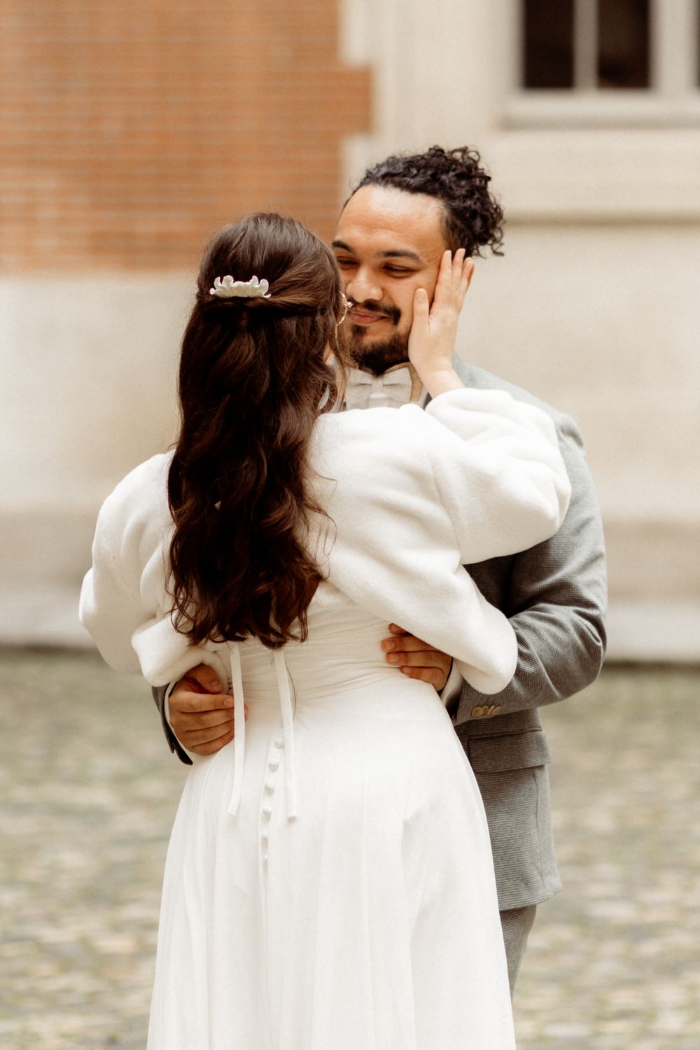 A romantic moment between newlyweds as bride in white dress and groom in gray suit embrace on stone path.