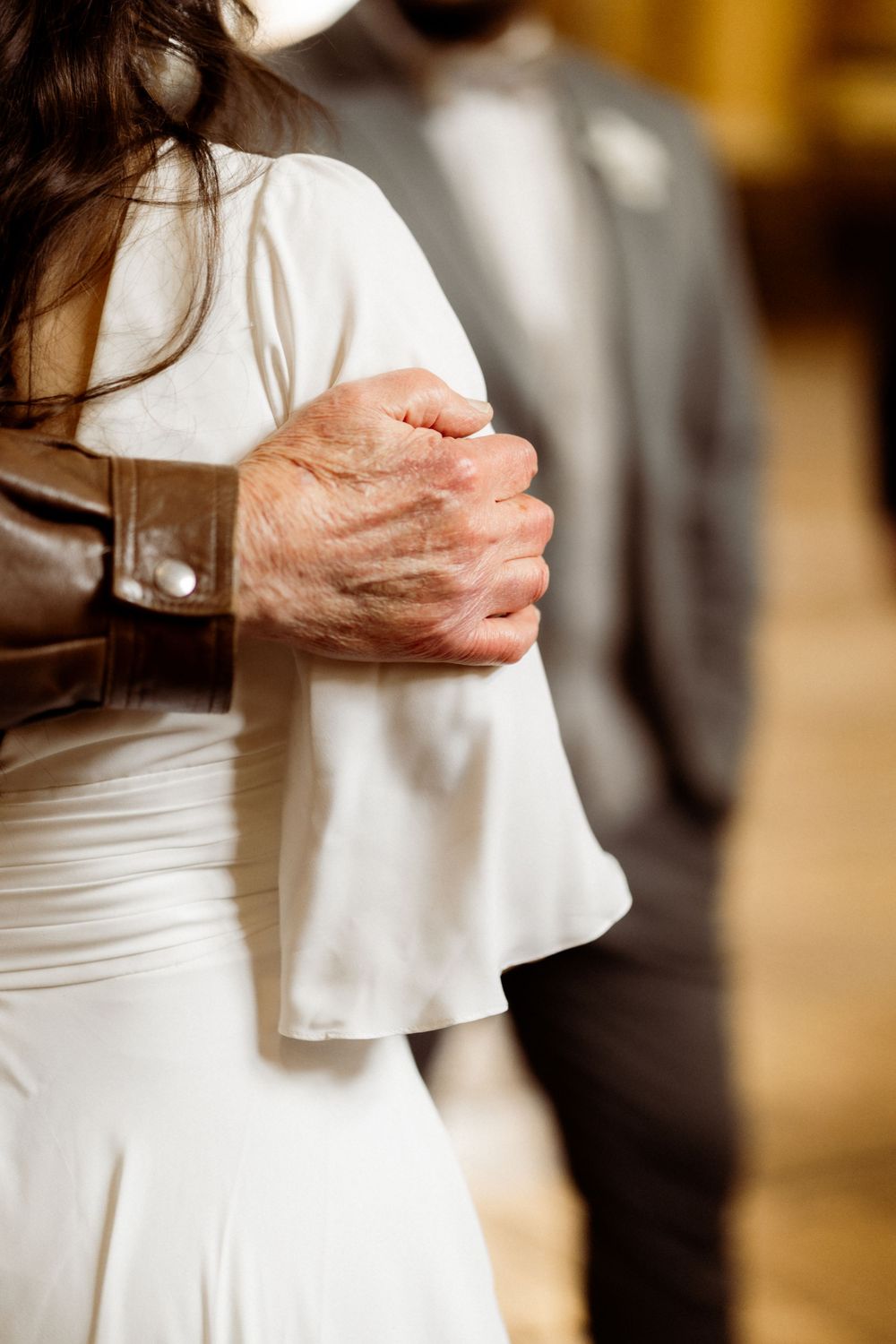 A close-up view of clasped hands during a wedding ceremony with a white dress visible in the foreground.