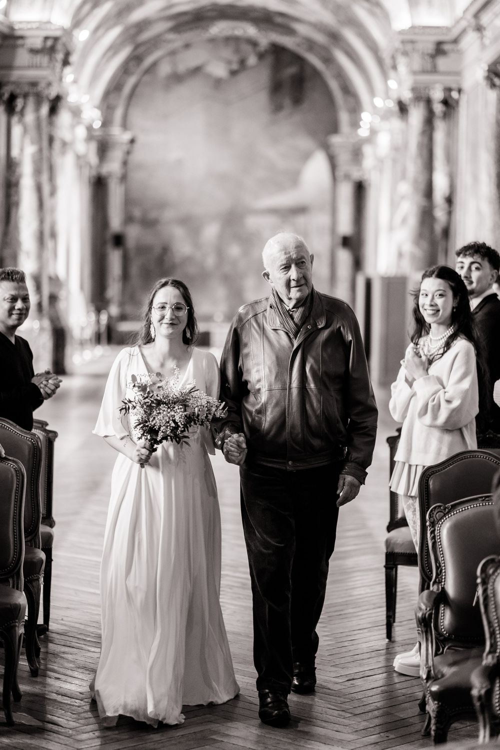Elderly couple laughing while walking together in an elegant hallway with ornate columns.