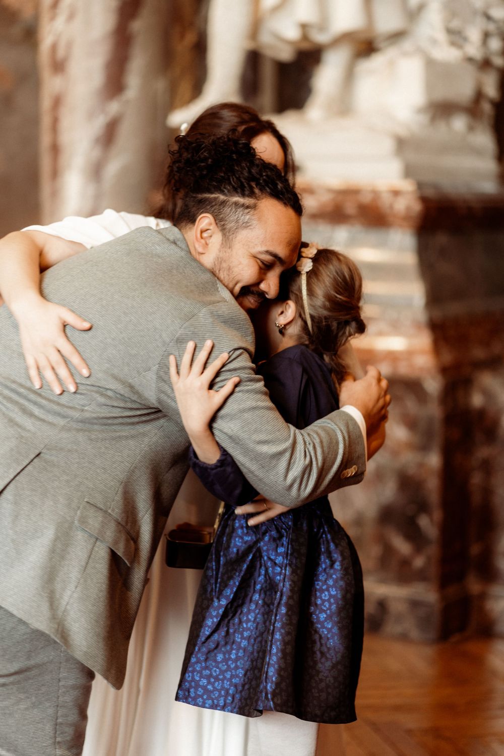 A couple in grey and blue attire embrace and kiss in a warmly lit indoor setting.