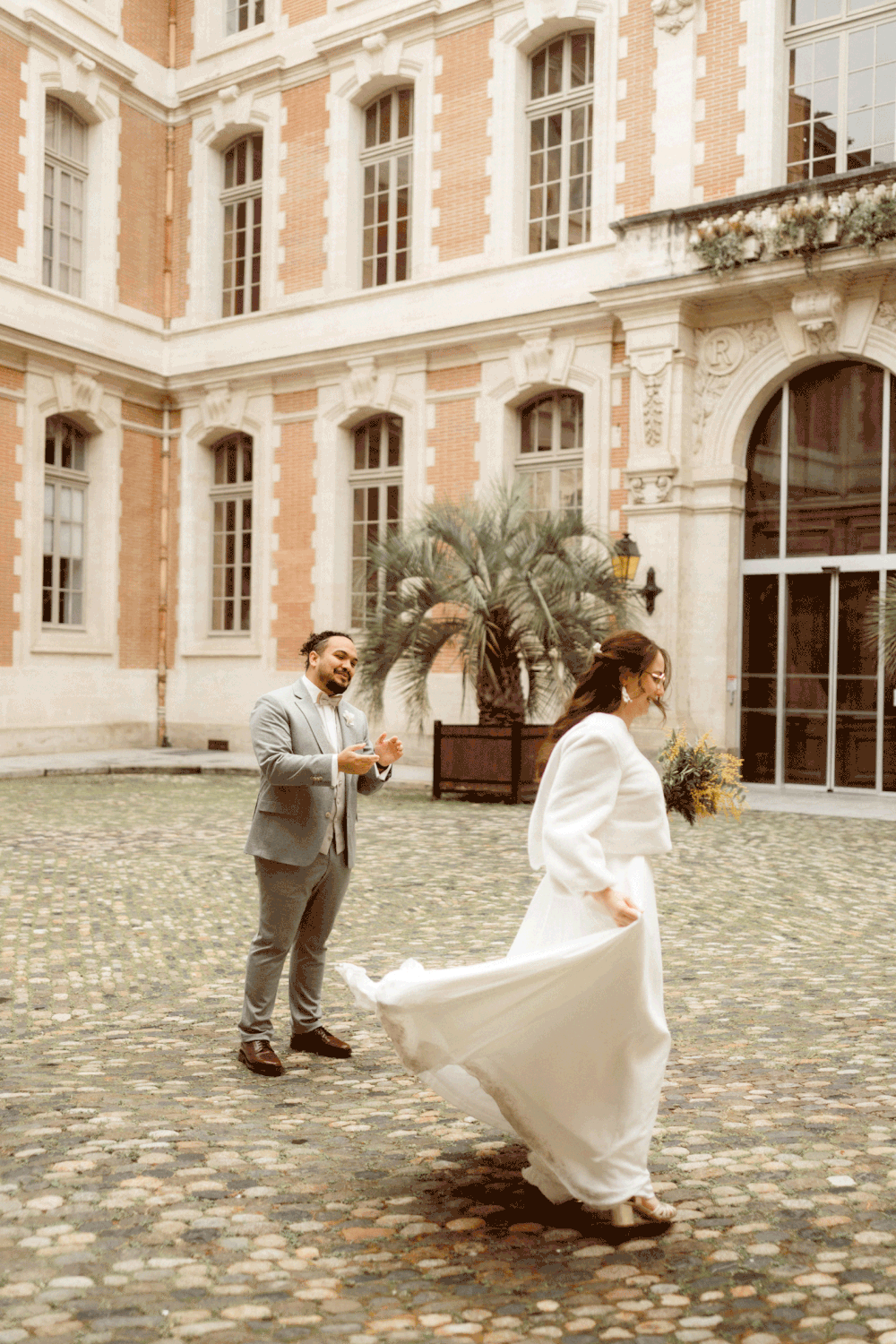 A couple shares a joyful moment in a historic courtyard with elegant architecture and cobblestone ground.