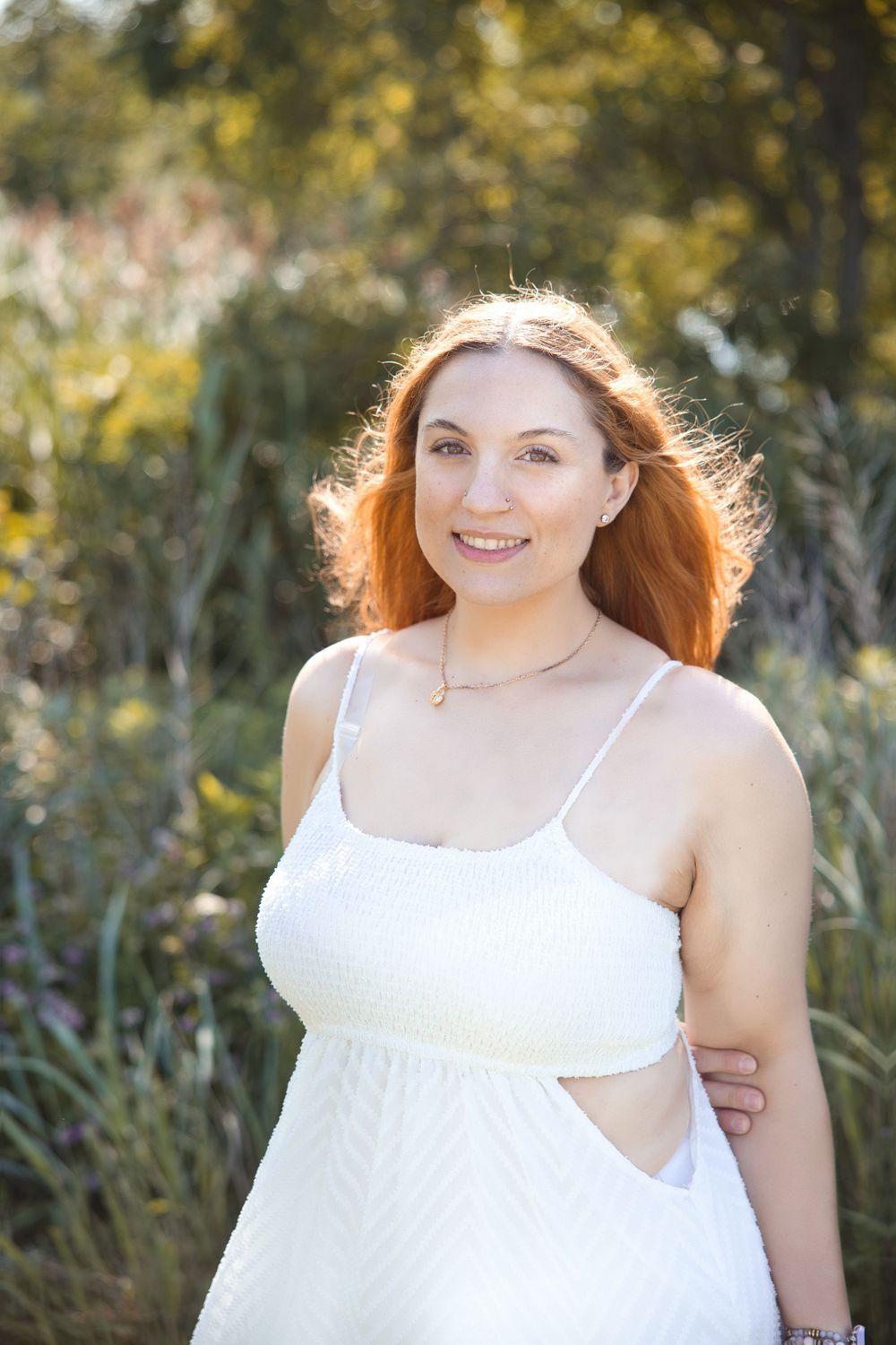 A woman with flowing red hair stands in a sunny field wearing a white summer dress.