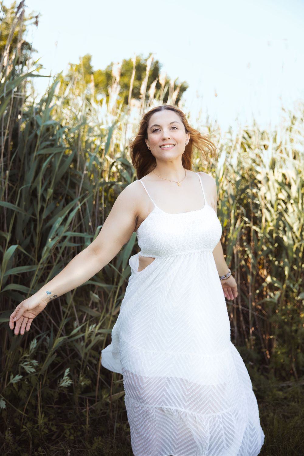 A white dress twirls elegantly against a backdrop of tall dried grass and reeds in golden sunlight.