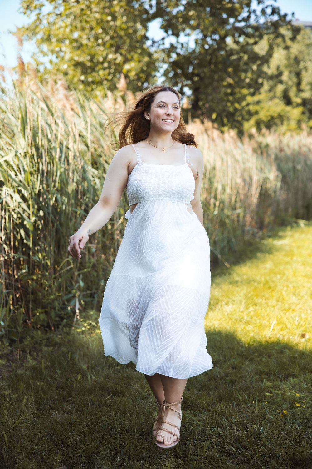 A flowing white summer dress catches movement in a sunny garden setting with tall grass and trees in the background.