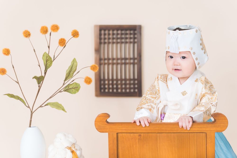 Child in traditional outfit exploring wooden furniture with orange flowers in background.