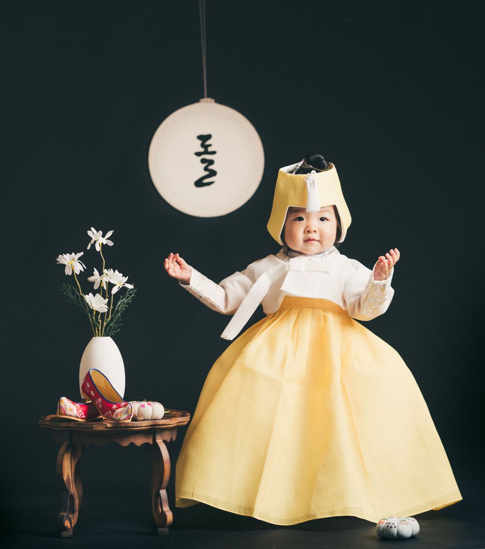 Child wearing yellow and white hanbok dress standing under a traditional Korean lantern.