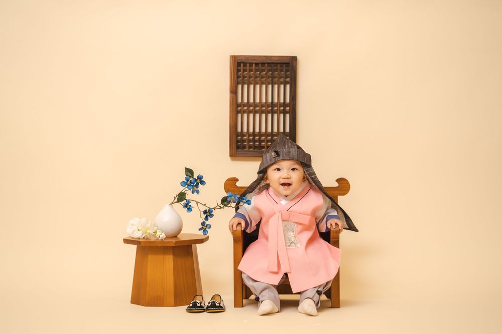 Child in pink traditional dress sitting in wooden chair with floral decorations.