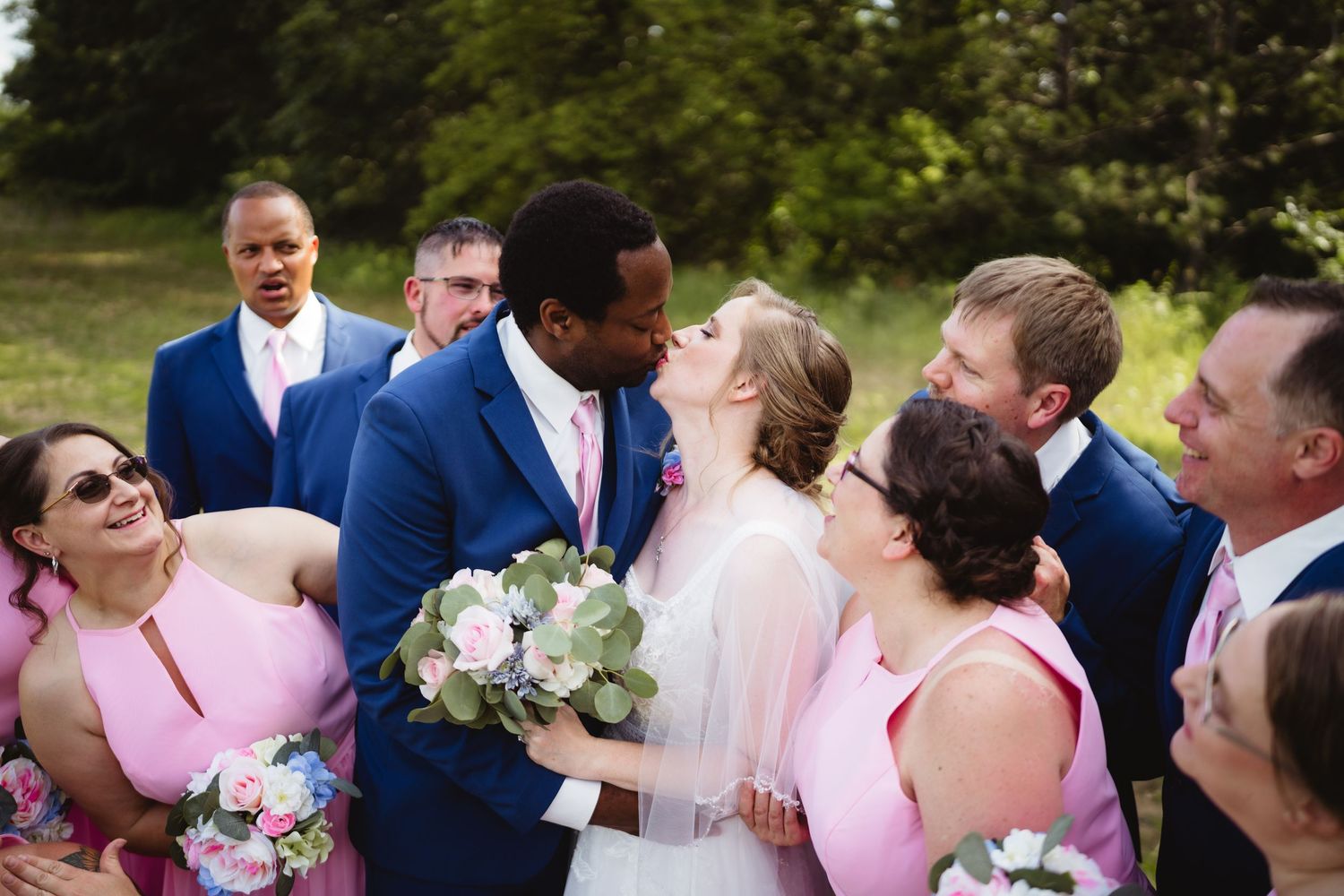 Wedding party gathering outdoors with bridesmaids in pink dresses and groomsmen in navy suits.