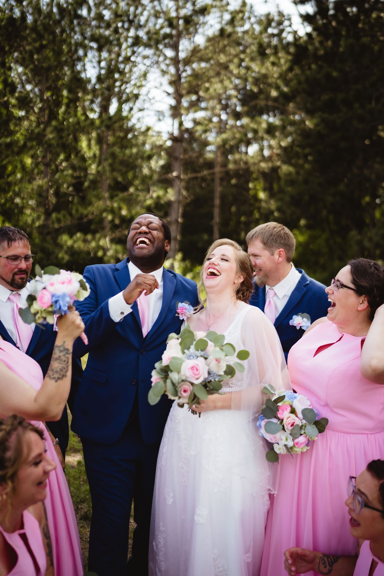 Wedding party in navy and pink attire share a joyful laugh together during outdoor celebration.