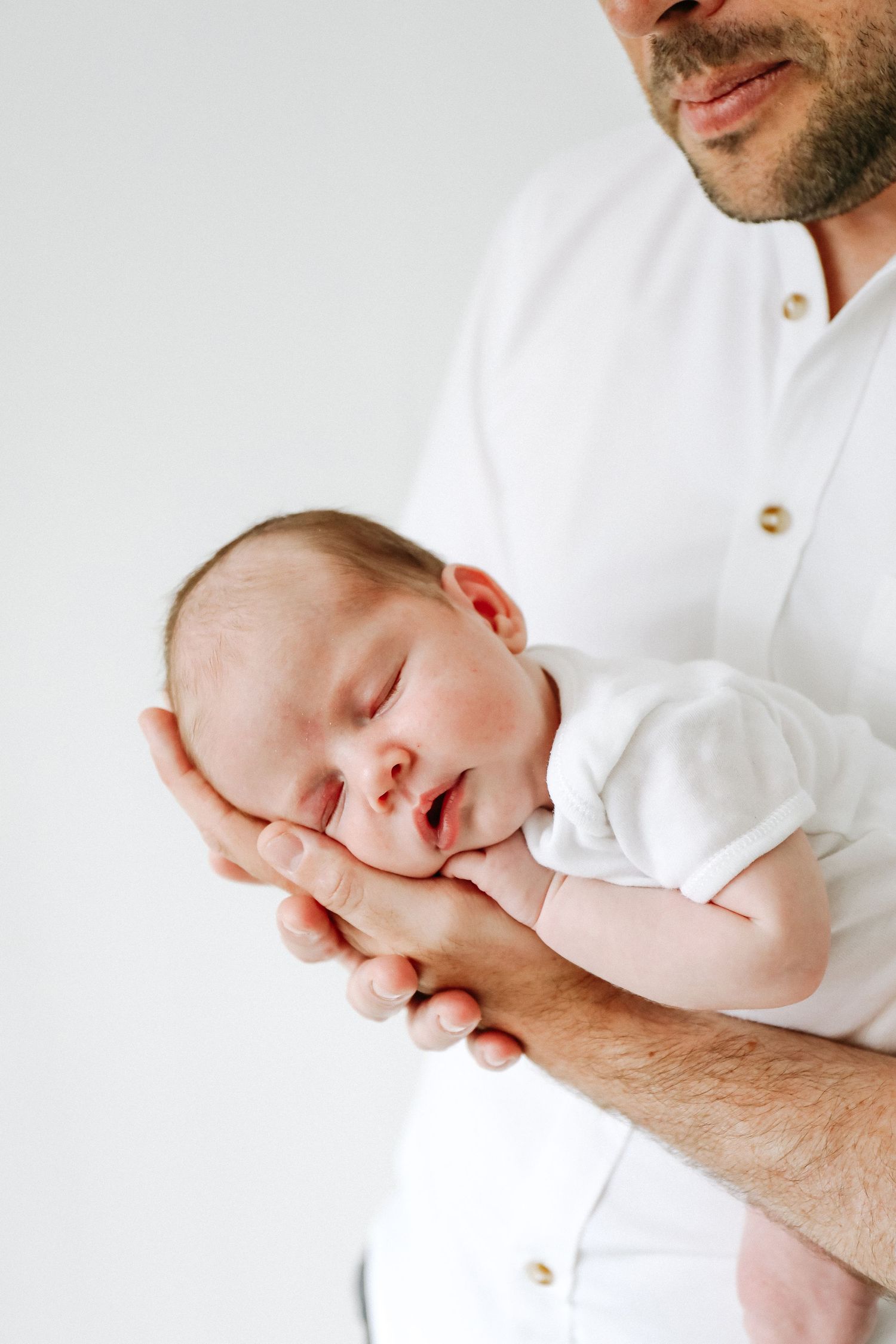 A sleeping newborn baby rests peacefully in their father's protective arms, during newborn photoshoot in Nottingham