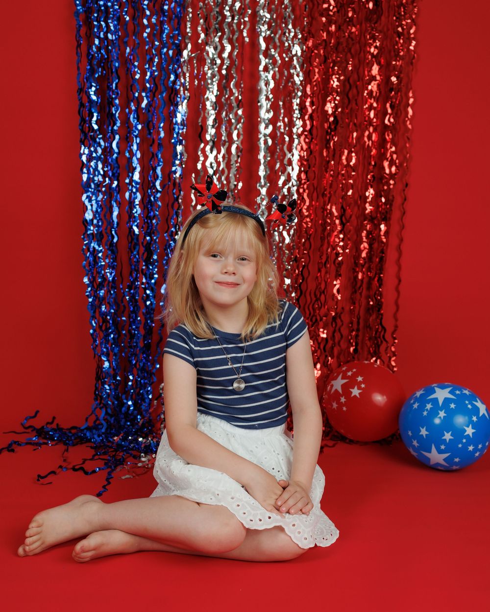 A patriotic studio portrait with red white and blue decor featuring sequined backdrop and balloons on a red floor.