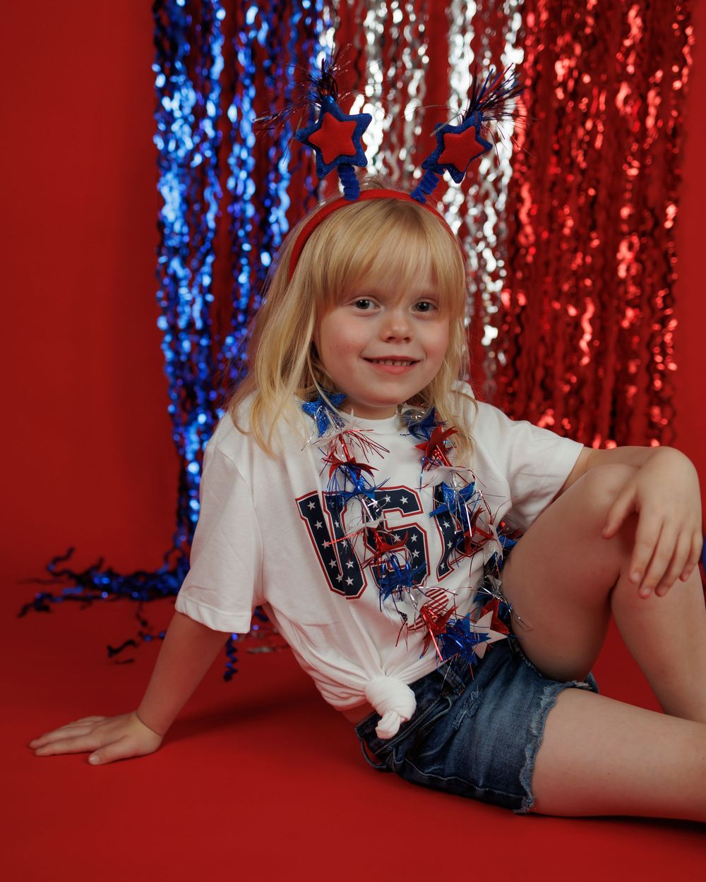 A child in a navy dress with red and blue sparkly backdrop poses in a series of playful positions on the floor.
