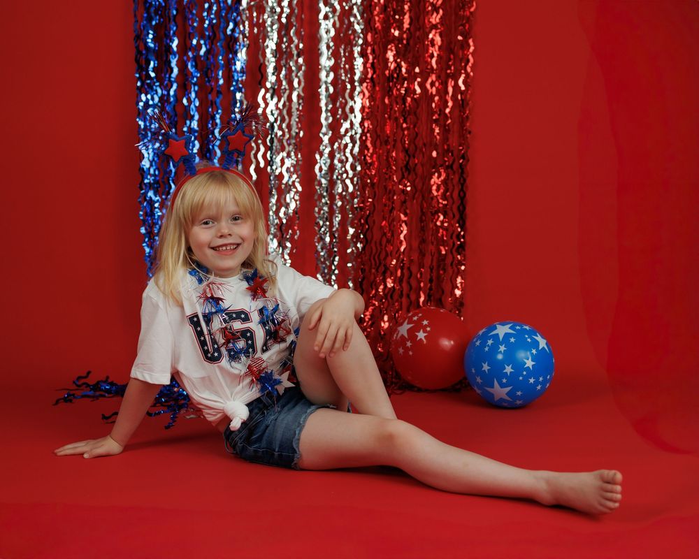 Child in a festive red and blue studio setting with sparkly curtains and balloons showing playful poses.