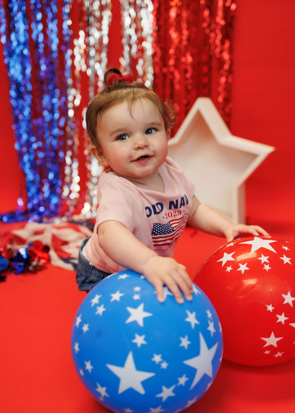 A patriotic photoshoot setup with a blue star balloon, red background, and sparkly decorations.