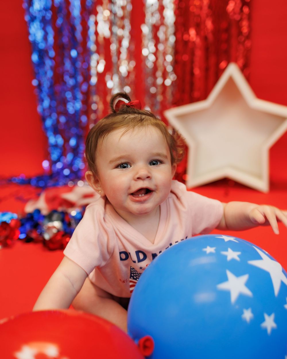 Patriotic holiday setting with red white and blue decor featuring balloons and sparkly tinsel backdrop with illuminated star.