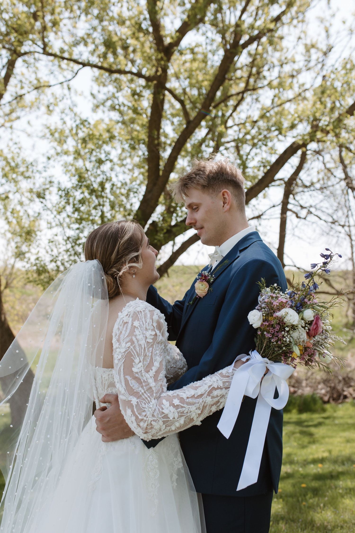 A bride and groom share a romantic moment outdoors, surrounded by trees and greenery.