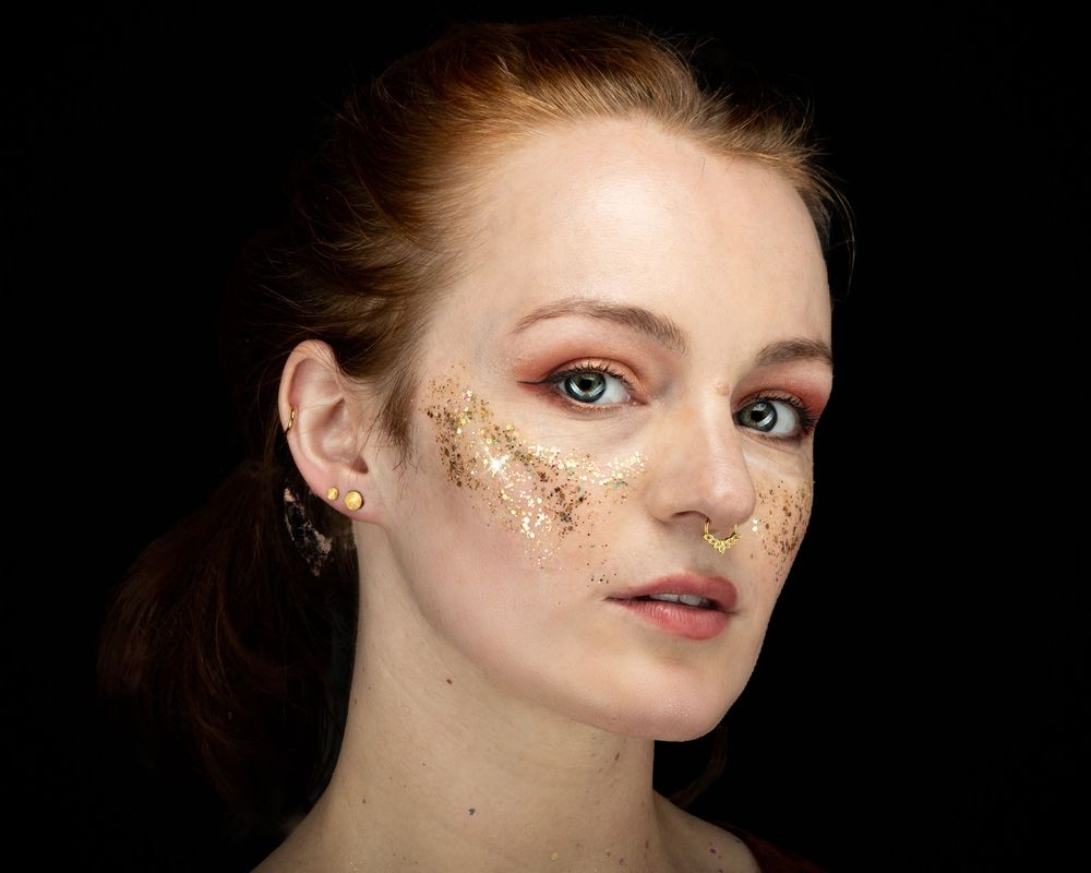 Creative beauty portrait with gold leaf makeup and glitter highlighting artistic eye and facial embellishments.