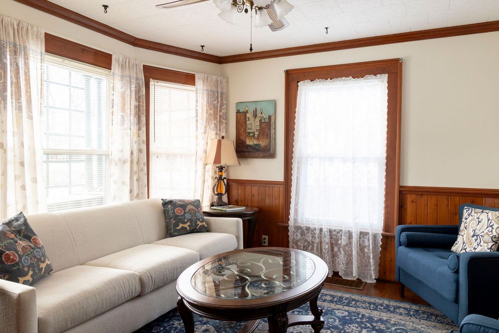 Elegant living space with lace curtains, wooden trim, and comfortable seating around a glass coffee table.
