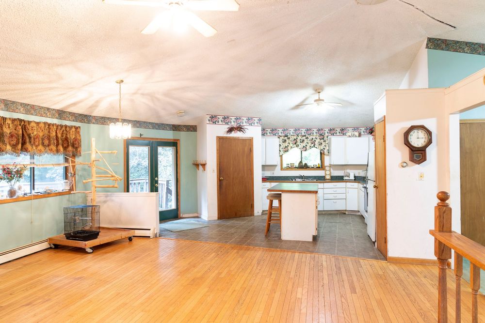 Large open living space with hardwood floors and exposed ceiling beams showing different angles of the room.