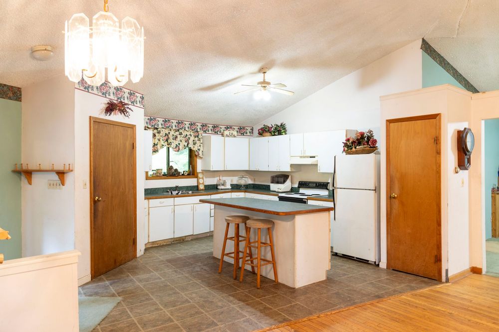 Modern white kitchen with island, tile flooring and chandelier lighting.