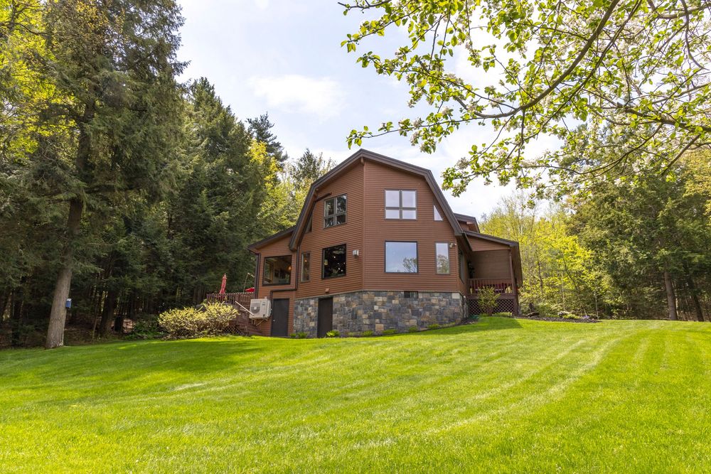 Exterior view of a brick house set on a sprawling green lawn surrounded by trees.