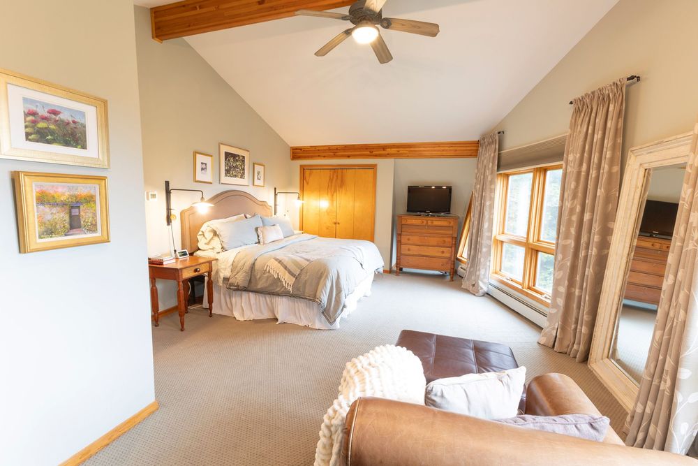 Bright bedroom with vaulted ceiling and large windows showcasing different angles of the space.
