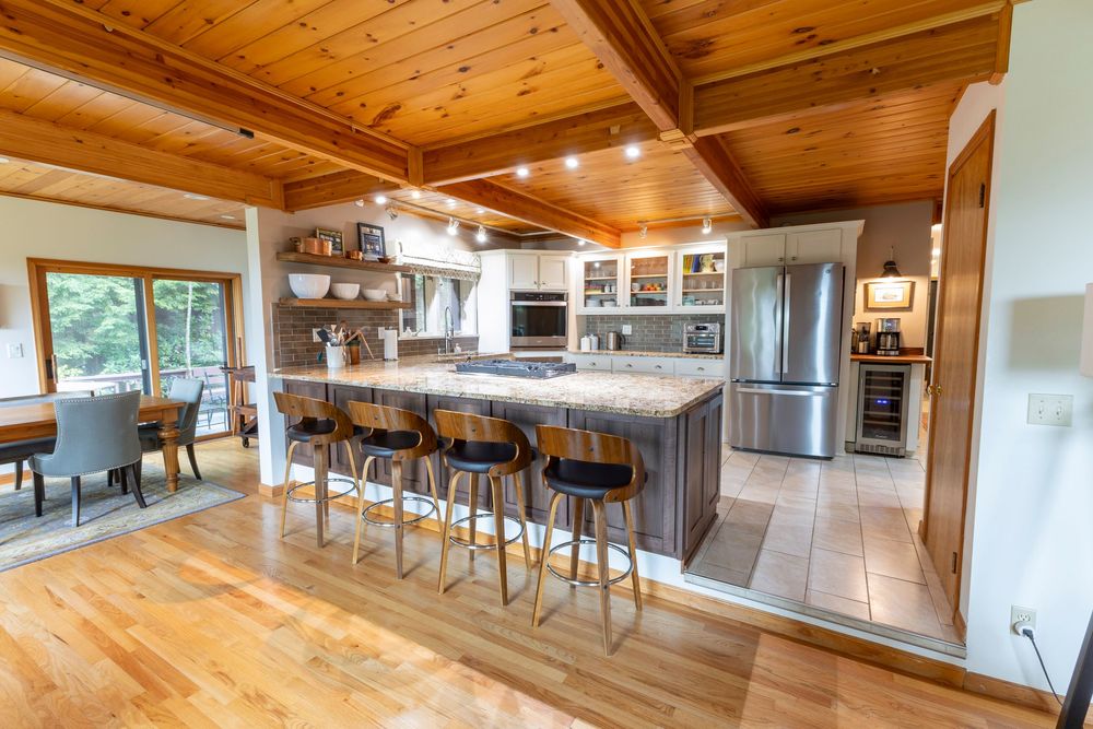 Open concept living area with wooden ceiling beams and modern furniture shown in panoramic view.