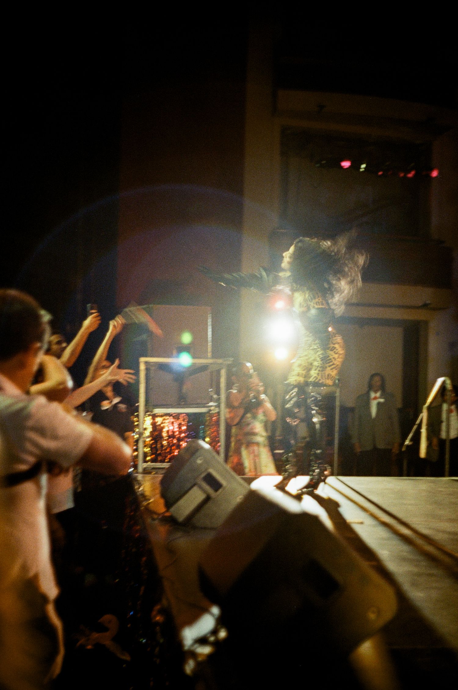 Energetic performer leaps high on stage during a dark concert with crowd reaching upward and stage lights illuminating.