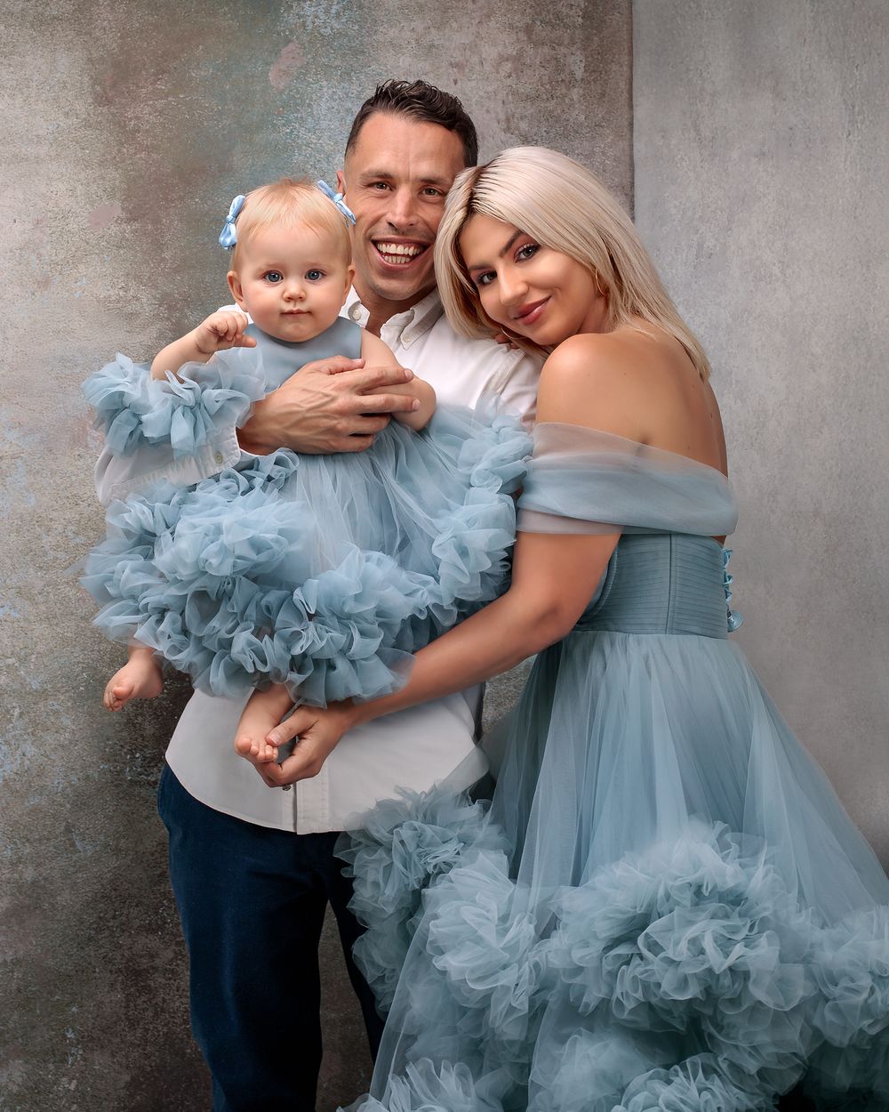 Emotional studio moment: Father holds baby girl while mother embraces them both. Mummy and daughter in matching dresses.