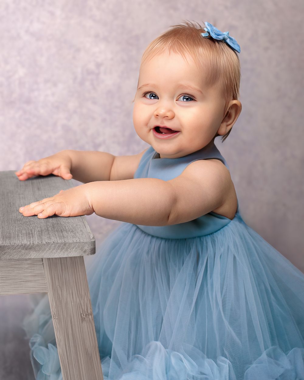 Baby girl in dusty blue dress and bow, by family studio photographer Caz Captures.