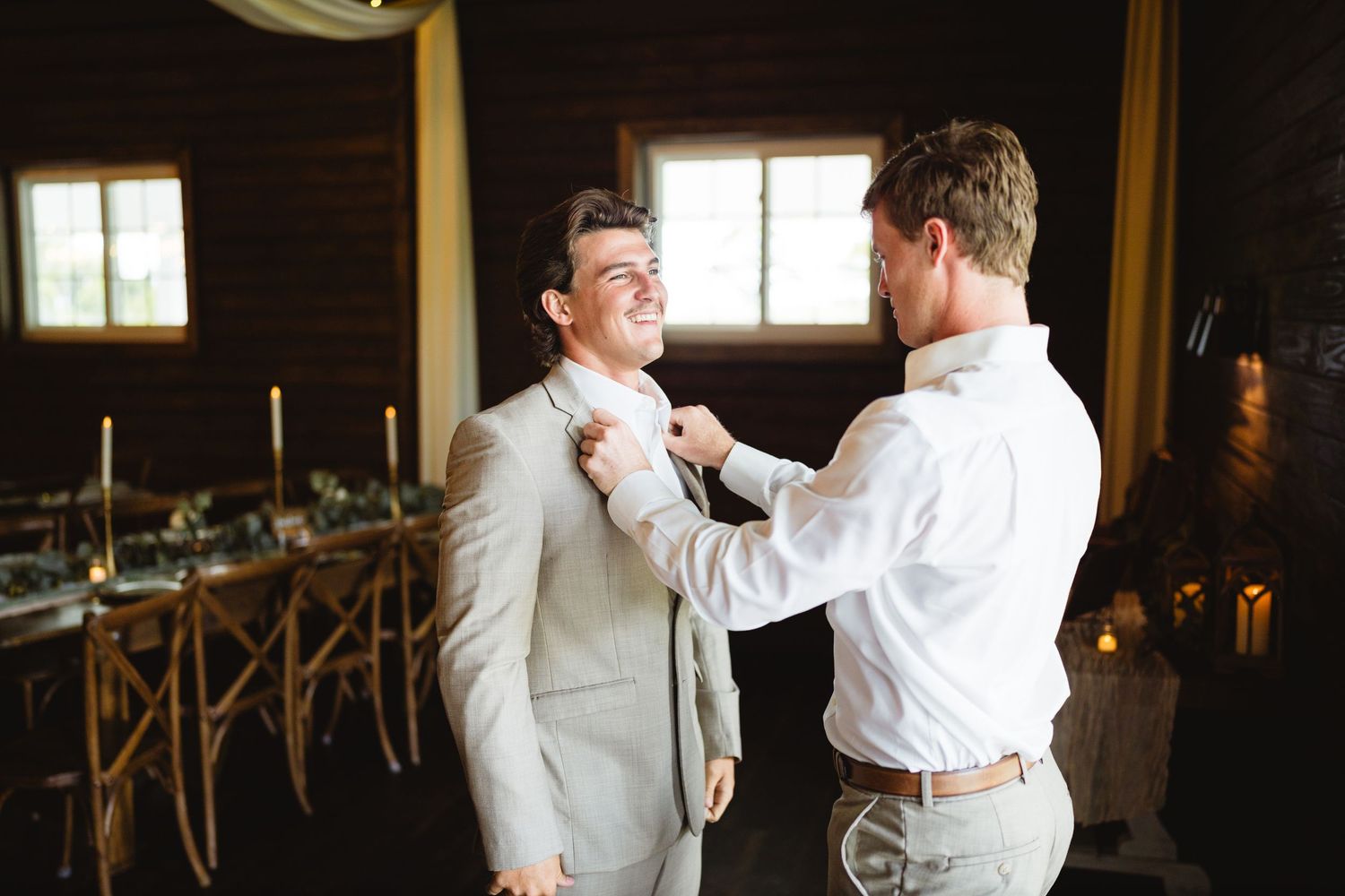 Two men in white dress shirts dance playfully in a dimly lit room as wedding preparations unfold.