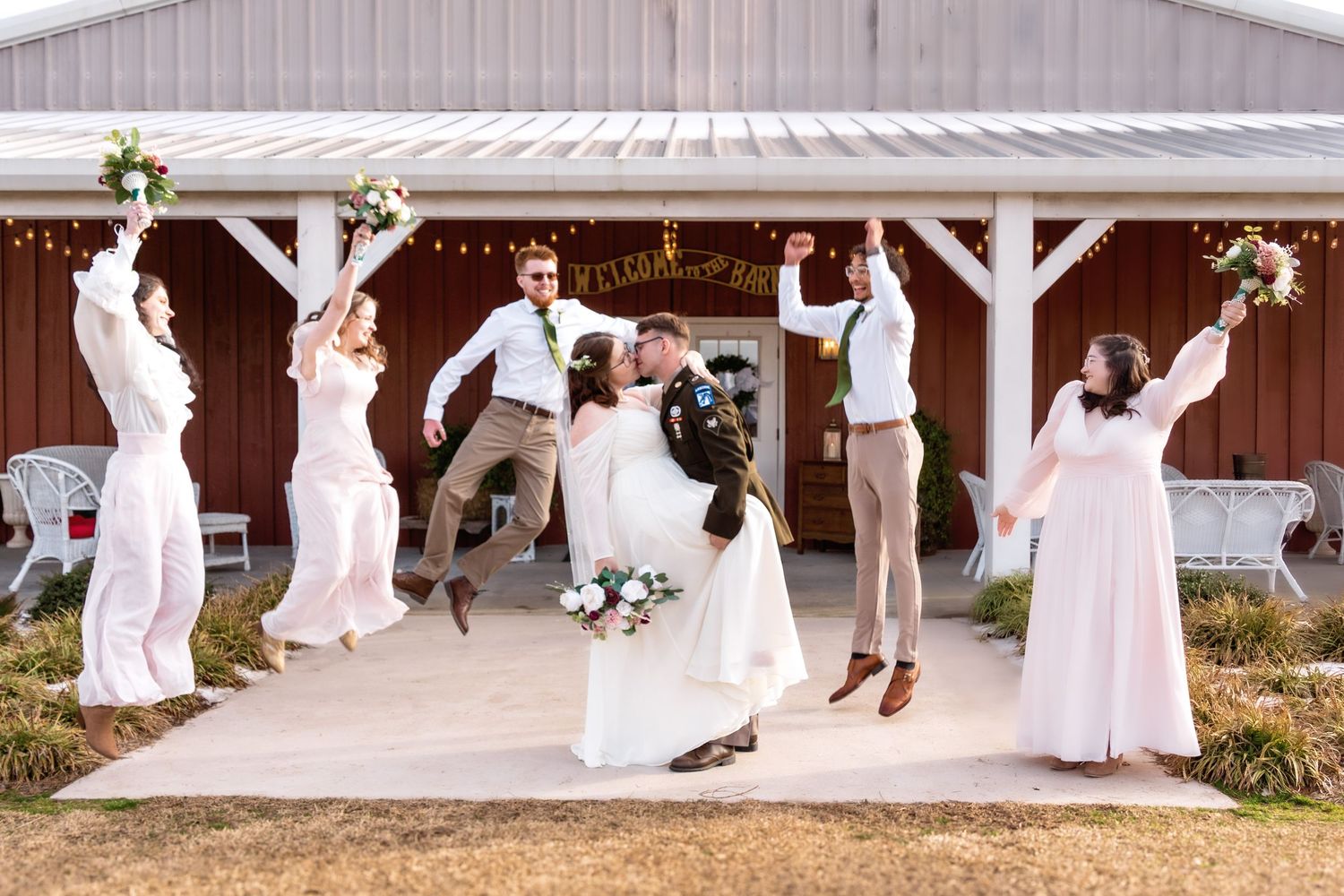 Wedding party jumps joyfully under a white gazebo decorated with floral arrangements.