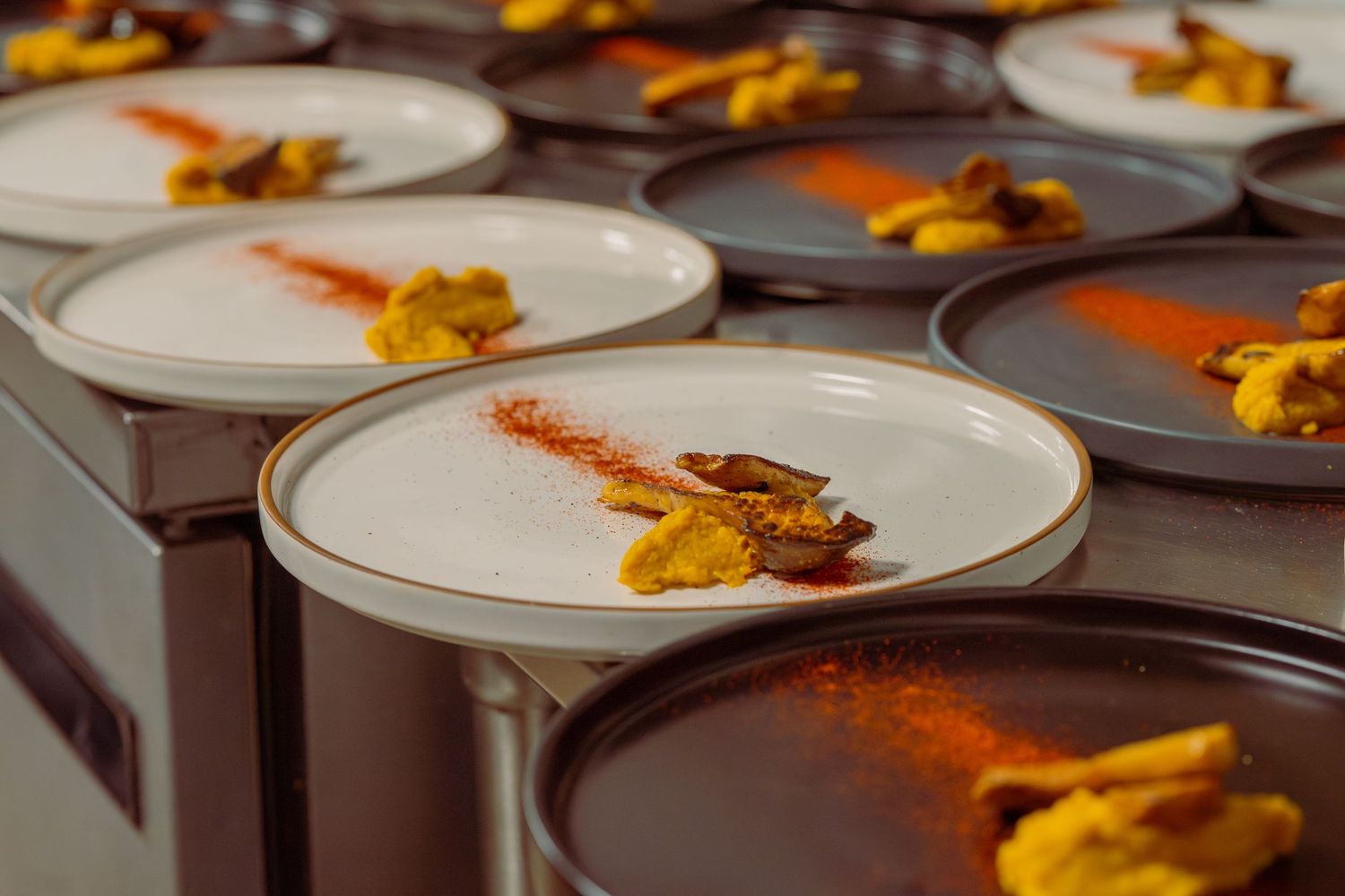 Golden curry sauce is carefully drizzled over white plates in an elegant dining presentation.